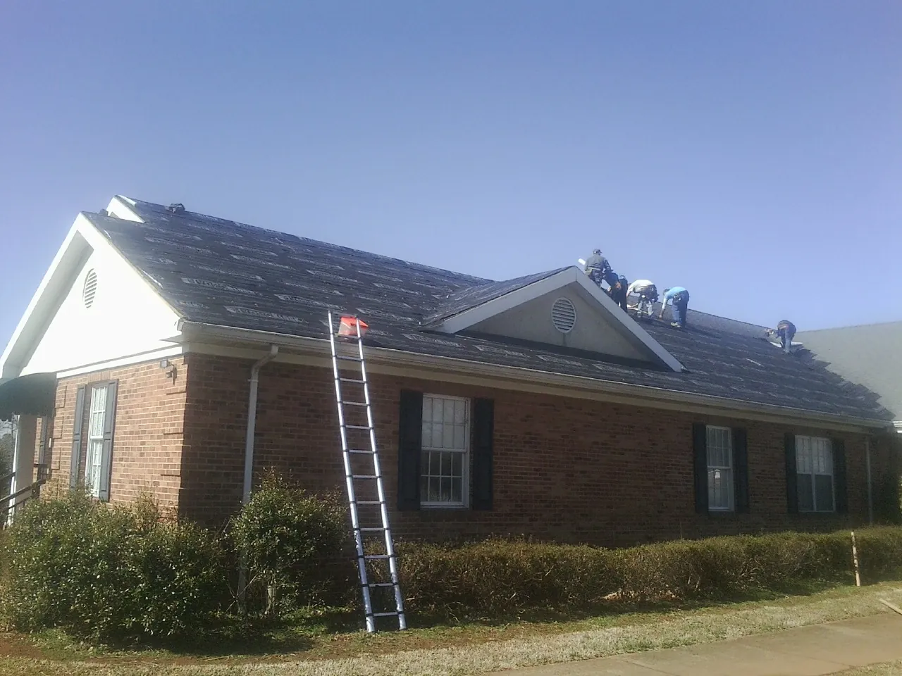 Crew tearing shingles off a brick ranch roof with a ladder set — Metal Roof Repair work by our crew in Breinigsville