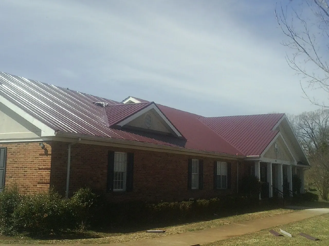 Red metal roof with gabled entries on a long brick building, from a Hail Damage Roof Repair job in Breinigsville