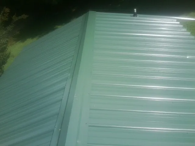 New green metal panels meeting at the ridge of a roof — Flat Roof Repair work by our crew in Breinigsville
