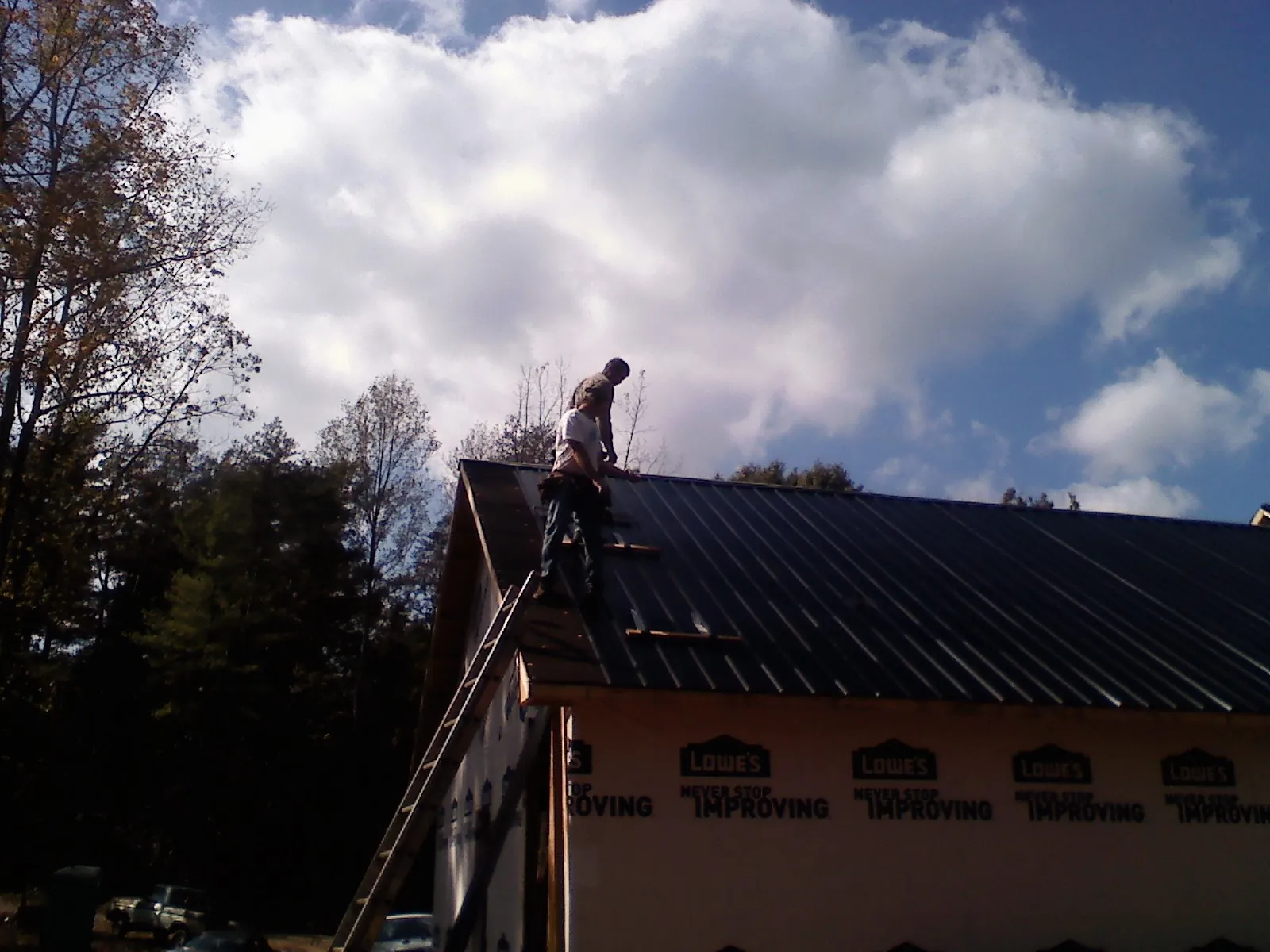 Roofer fastening dark metal panels high against a cloudy sky, from a Roof Inspection job in Breinigsville