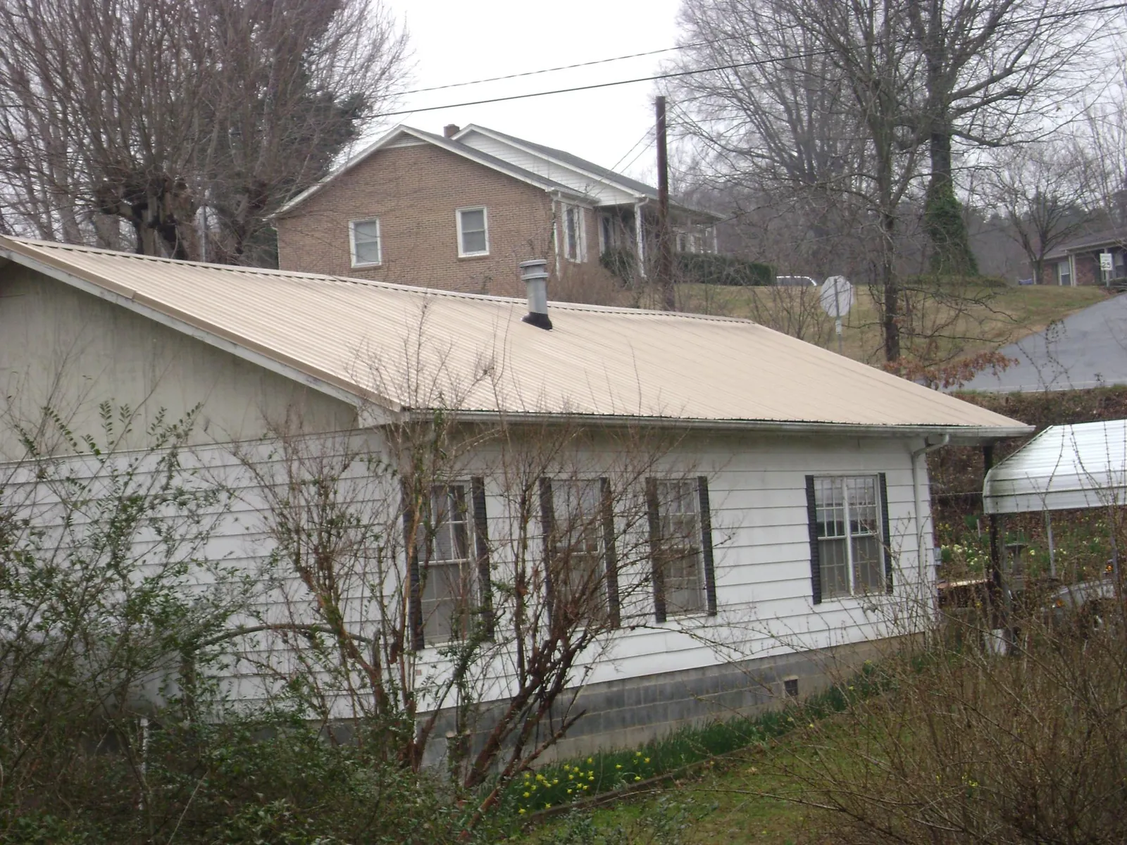 Tan metal roof on a white sided house set into a hillside — Commercial Roofing by Roofing Brothers in Breinigsville
